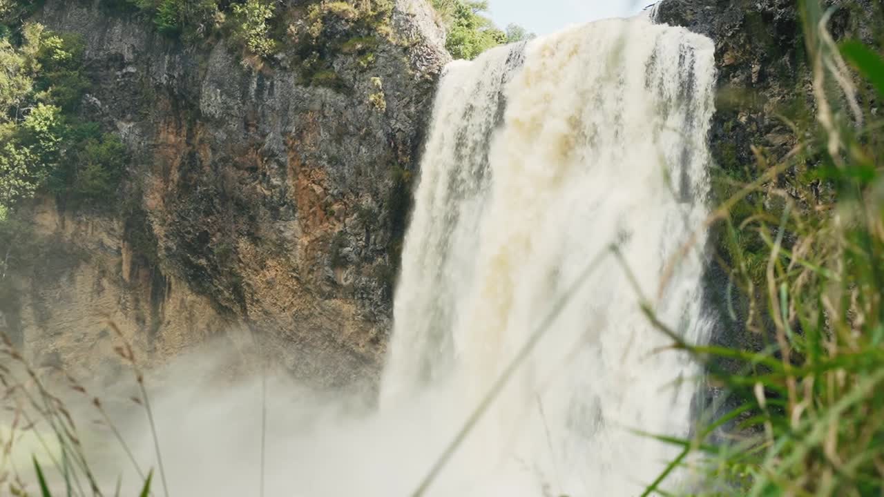 Strong waterfall crashes down rugged cliff surrounded by greenery in Faro, Portugal. Thick mist rises as water hits rocks below, creating dramatic and refreshing natural scene in summer light.
