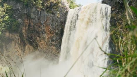 strong waterfall crashes down rugged cliff surrounded by greenery in faro, portugal. thick mist rises as water hits rocks below, creating dramatic and refreshing natural scene in summer light.