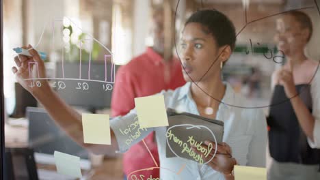 Happy-african-american-colleagues-taking-notes-on-glass-wall-and-discussing-work,-slow-motion