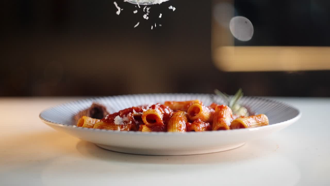 Close up view in slow motion of a Hand spreading grated Parmesan cheese over hot and smoky pasta dish under beautiful lighting