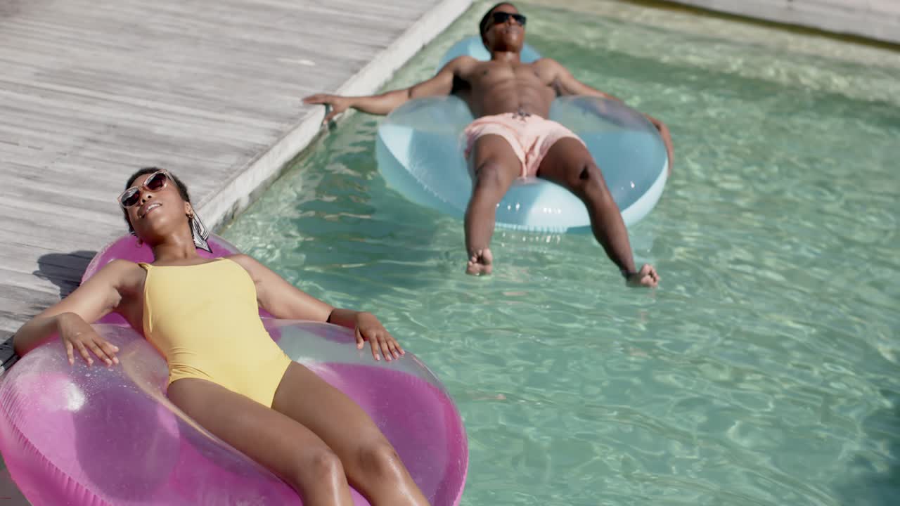 Woman reclining on pink float adjusting shades for ad, camera pulling back as man reaching deck