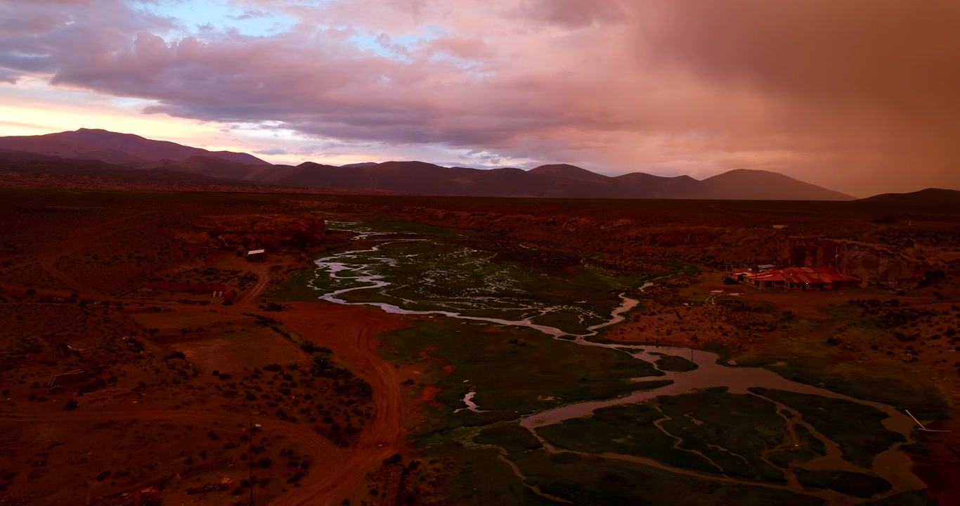 Remote village of Aguas Calientes in Bolivian Altiplano during dramatic and colorful sunset. Aerial forward, copy space