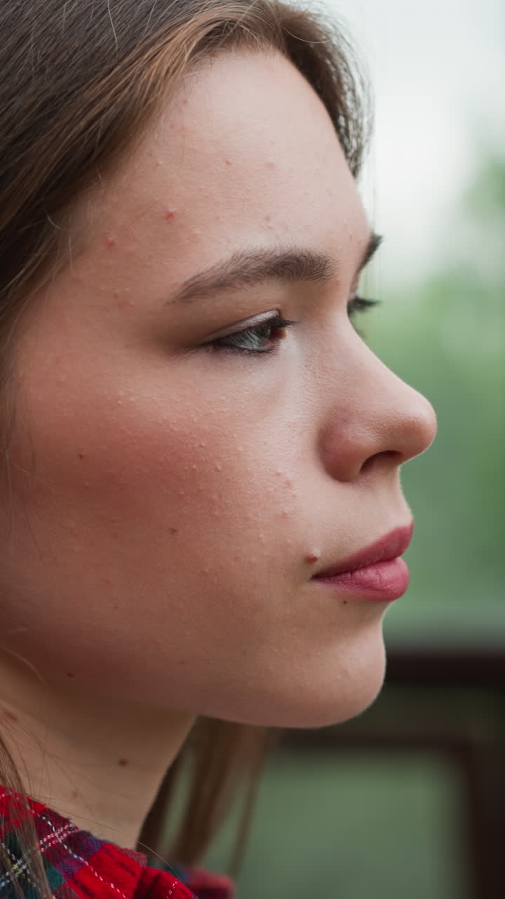 Serious woman stands in studio closeup. Pretty lady suffers from obsessive thoughts looking out of window on terrace. Mental health issues treatment