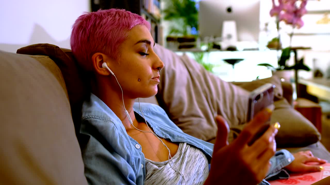 mujer de cabello rosa usando teléfono móvil en el sofá 4k