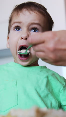 adorable toddler having meals. kid holds the fork but eats from mom's spoon. low angle view. vertical video