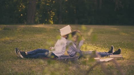 tired boys with textbooks rest on lush lawn grass in park