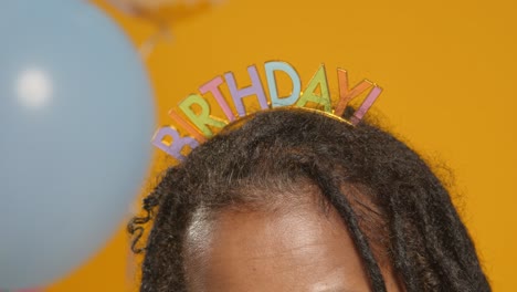 close up studio portrait of woman wearing birthday headband celebrating with balloons