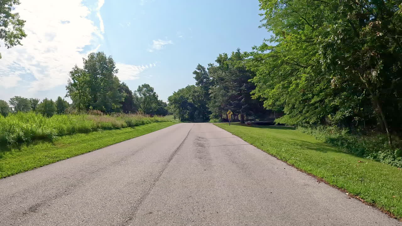 POV - driving on paved road thru Jester County Park in the Des Moines River Valley in central Iowa; driving past the one of the trailhead parking areas and a large meadow; vacation, holiday