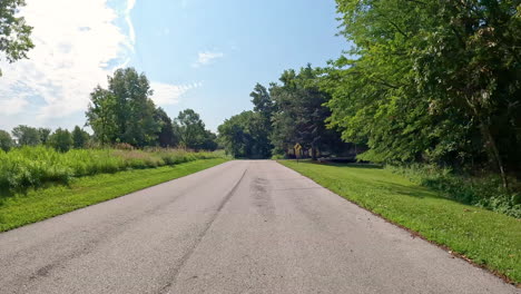 pov - driving on paved road thru jester county park in the des moines river valley in central iowa; driving past the one of the trailhead parking areas and a large meadow; vacation, holiday