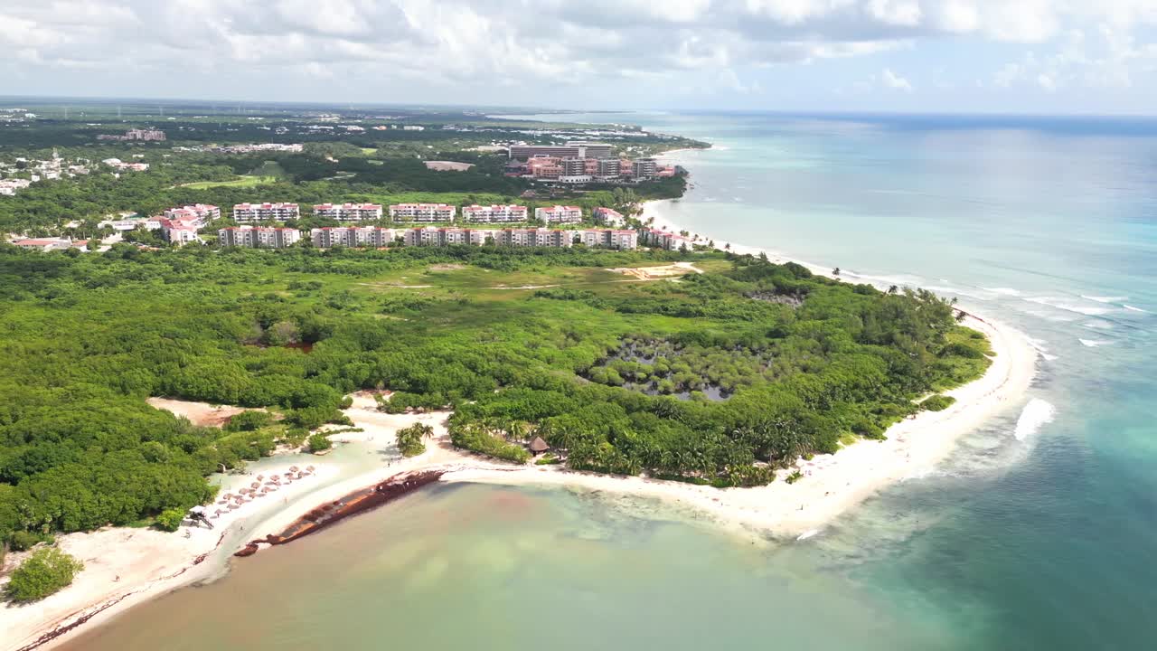 Drone footage flying above the coastline of Mexico’s Riviera Maya, capturing resort buildings, beach, turquoise sea and lush coastal vegetation for travel and tourism use