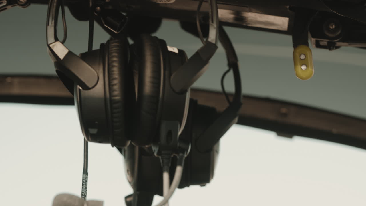 Headphones hang from the cockpit of a military helicopter, indicating active communications during a mission. The interior of the aircraft is visible, showcasing military operations.