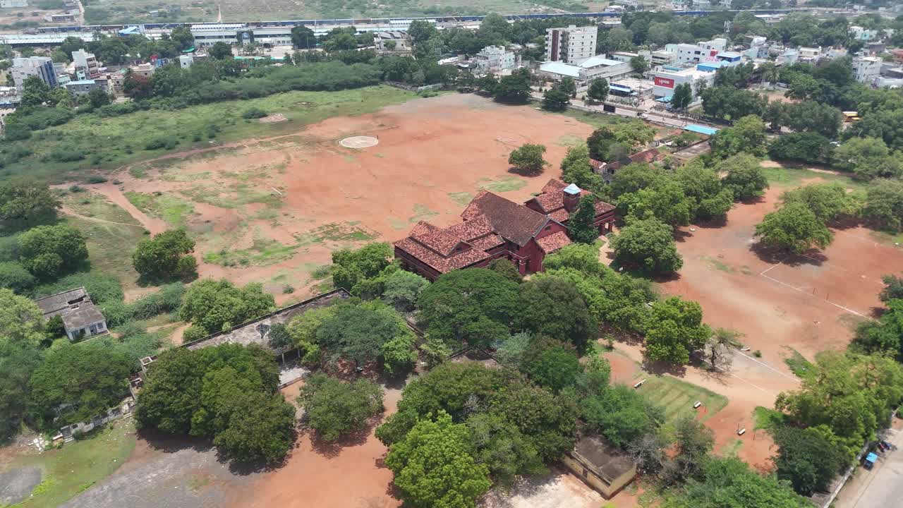 Aerial Drone Shot of Red Building near Open ground with tree surrounded in the city.