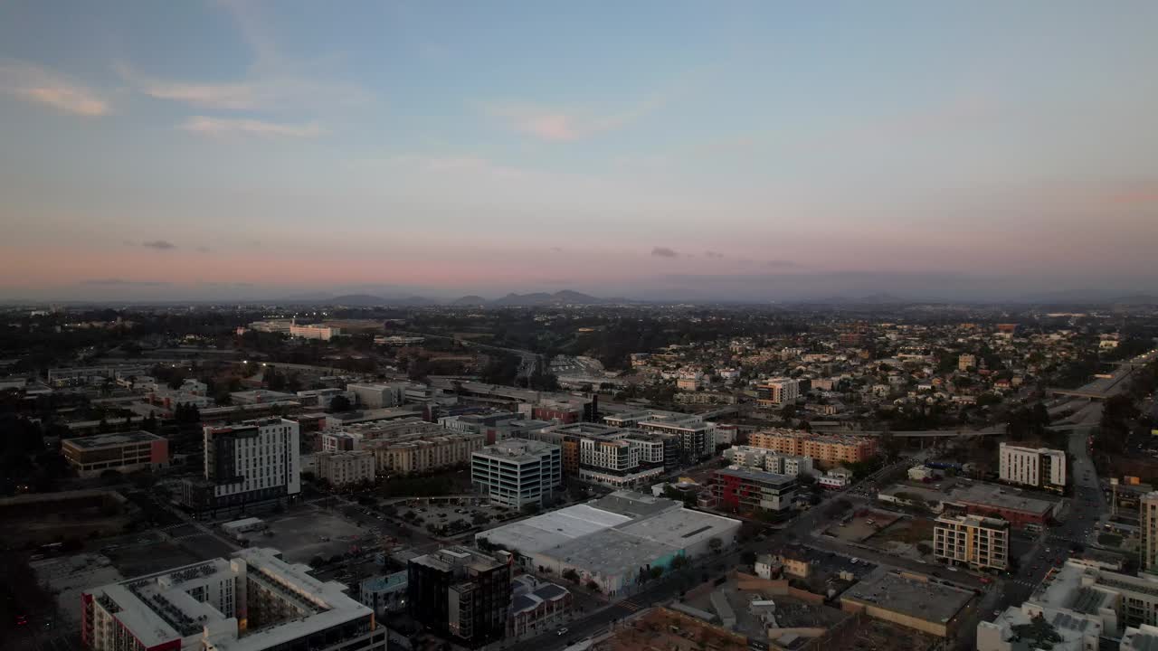 Drone flyver mod Interstate 5 nær centrum af San Diego ved solnedgang med bjerge synlige i baggrunden.