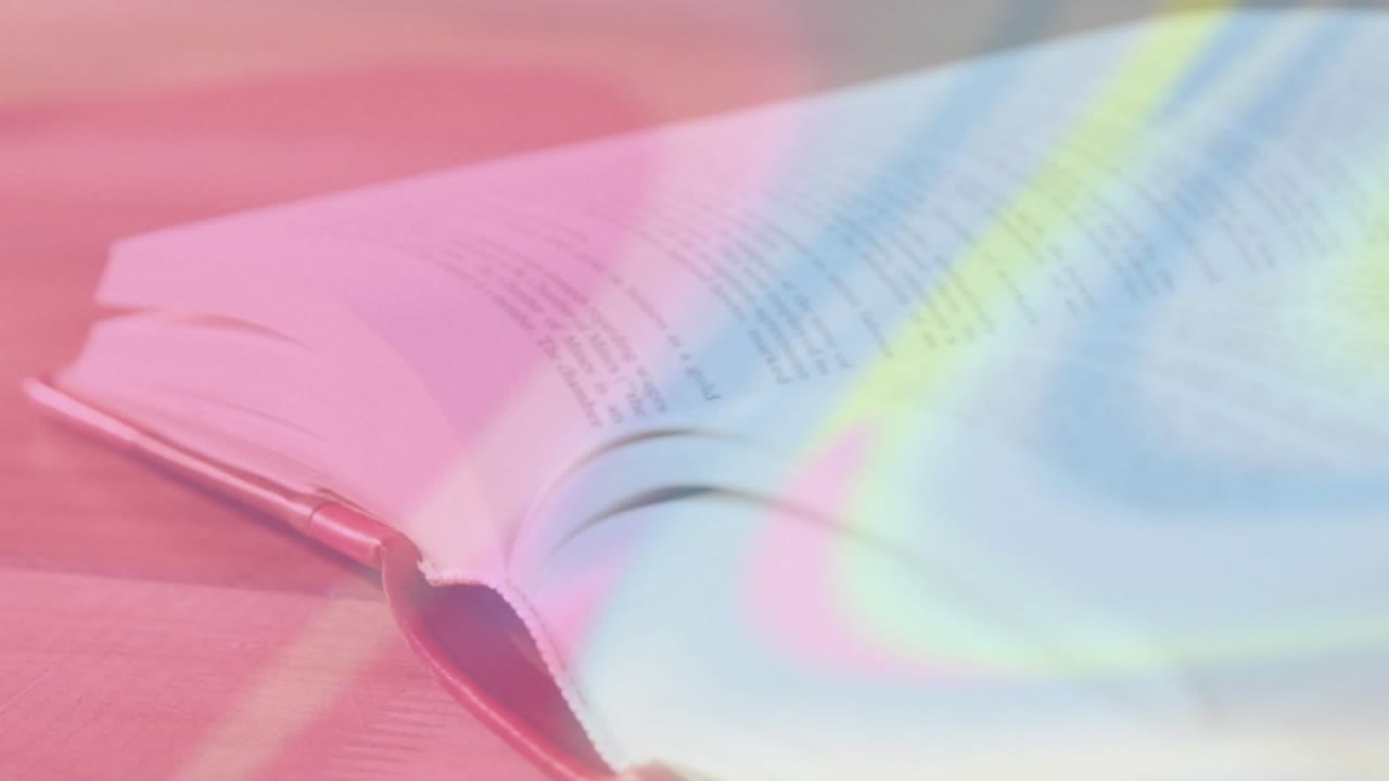 Morbide proiezioni di luce pastello colpiscono un libro aperto su una scrivania di legno, sfogliando le pagine e una sovrapposizione che si trasforma.