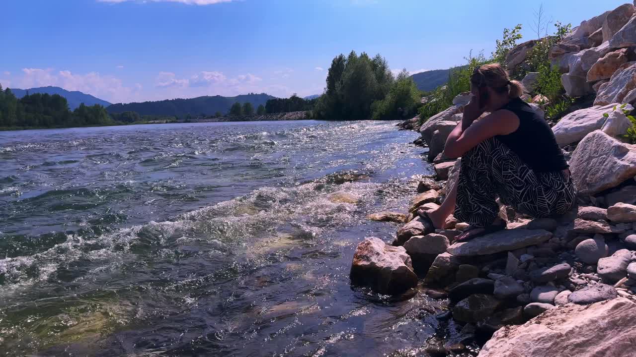 A Reflective Moment by the River: A Woman Contemplates Life by the Water's Edge Amidst the Serenity of Nature and Flowing Waters Under a Sunny Sky