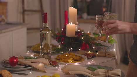 unrecognizable woman putting two champagne glasses on christmas dinner table