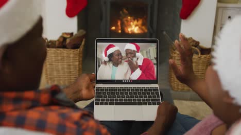 Afroamerikanisches-Paar-Mit-Weihnachtsmützen-Nutzt-Laptop-Für-Weihnachtsvideoanruf-Mit-Paar-Auf-Dem-Bildschirm