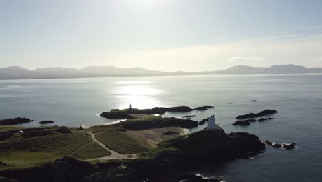 Aerial-view-towards-idyllic-Ynys-Llanddwyn-island-with-hazy-Snowdonia-mountain-range-across-shimmering-Irish-sea-at-sunrise