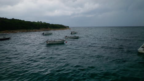 Aerial-trucking-pan-across-rocky-ocean-ripples-above-small-boats-anchored-off-coastline