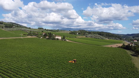 Tractor-Amarillo-Trabajando-En-Las-Estrechas-Hileras-De-Viñedos-Verdes-Bajo-El-Hermoso-Cielo-En-Las-Colinas-Toscanas,-Chianti-Frescobaldi,-Italia