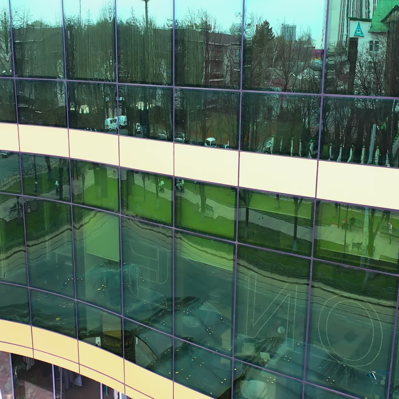 Exterior of the modern glass building reflecting cityscape. Aerial shot of beautiful financial center with reflective glass walls outside. Camera moves top down.