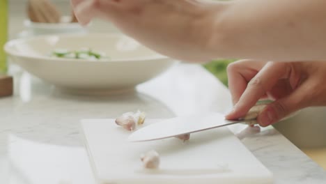 Woman-crushing-garlic-on-wooden-board-in-kitchen