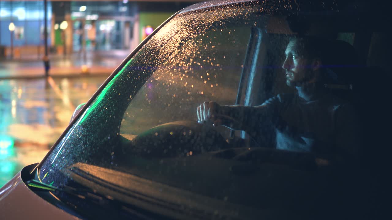 비가 오는 저녁에 차에 앉아 있는 젊은 남자