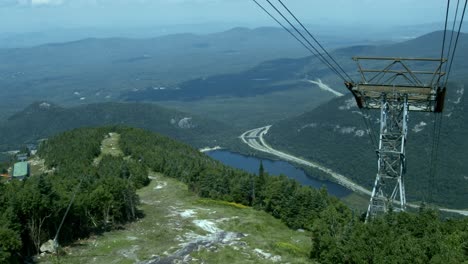 The-camera-descends-an-aerial-tramway-looking-over-a-ski-slope-and-cable-tower-with-a-mountain-range-in-the-distance