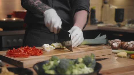 puerro verde fresco cortado en una tabla de madera por un joven chef profesional con un elegante pantalones negro con tatuajes