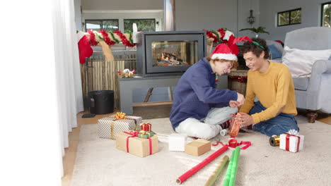 diverse gay male couple wrapping christmas presents by fireplace at home, slow motion, copy space