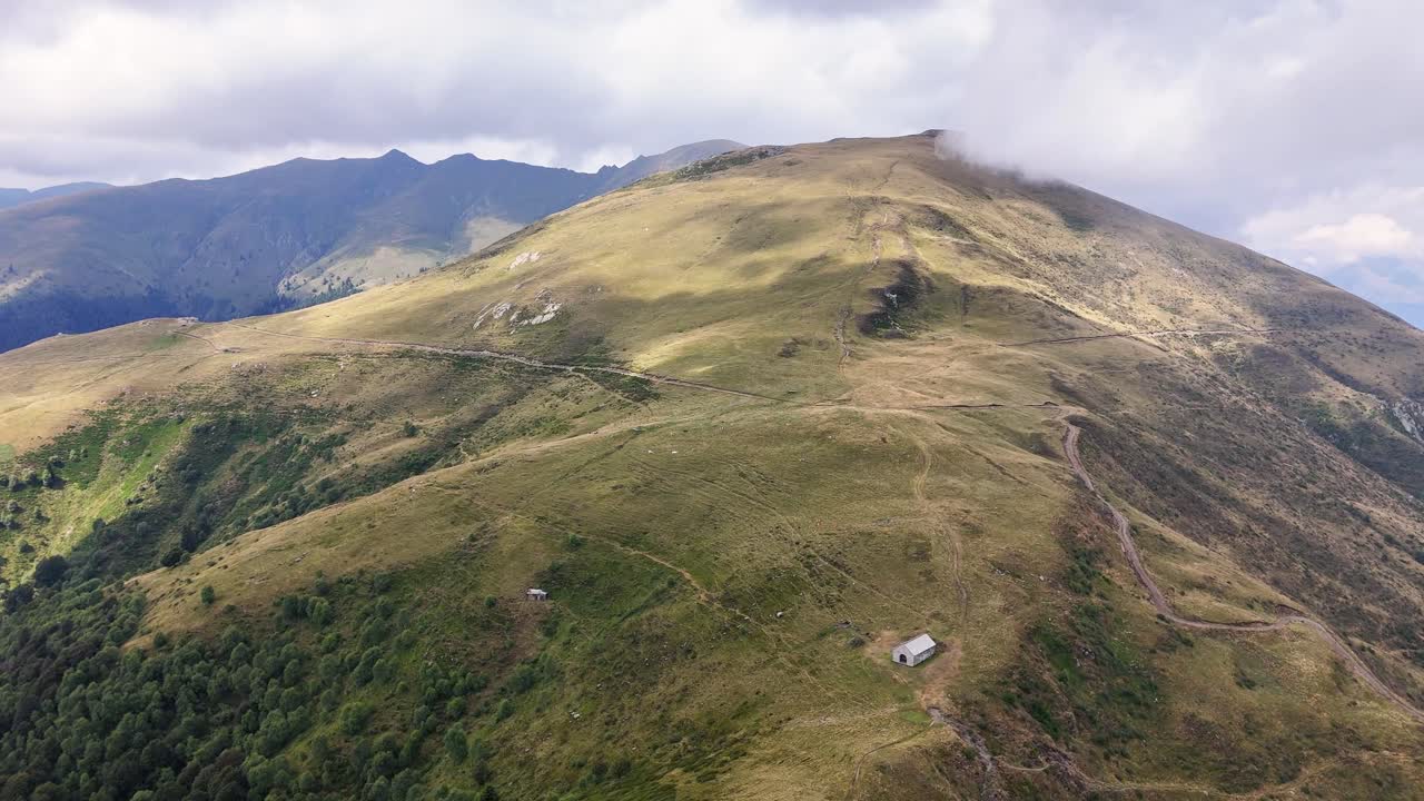 Scatto aereo ad angolo elevato della cima del Monte Grona nelle Prealpi lombarde con sentieri escursionistici che si snodano su pendii erbosi verso la vetta, offrendo viste sulle montagne circostanti e sul paesaggio vicino al Lago di Como