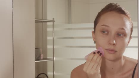 chica masajeando su cara con un masajeador de goma mirando al espejo