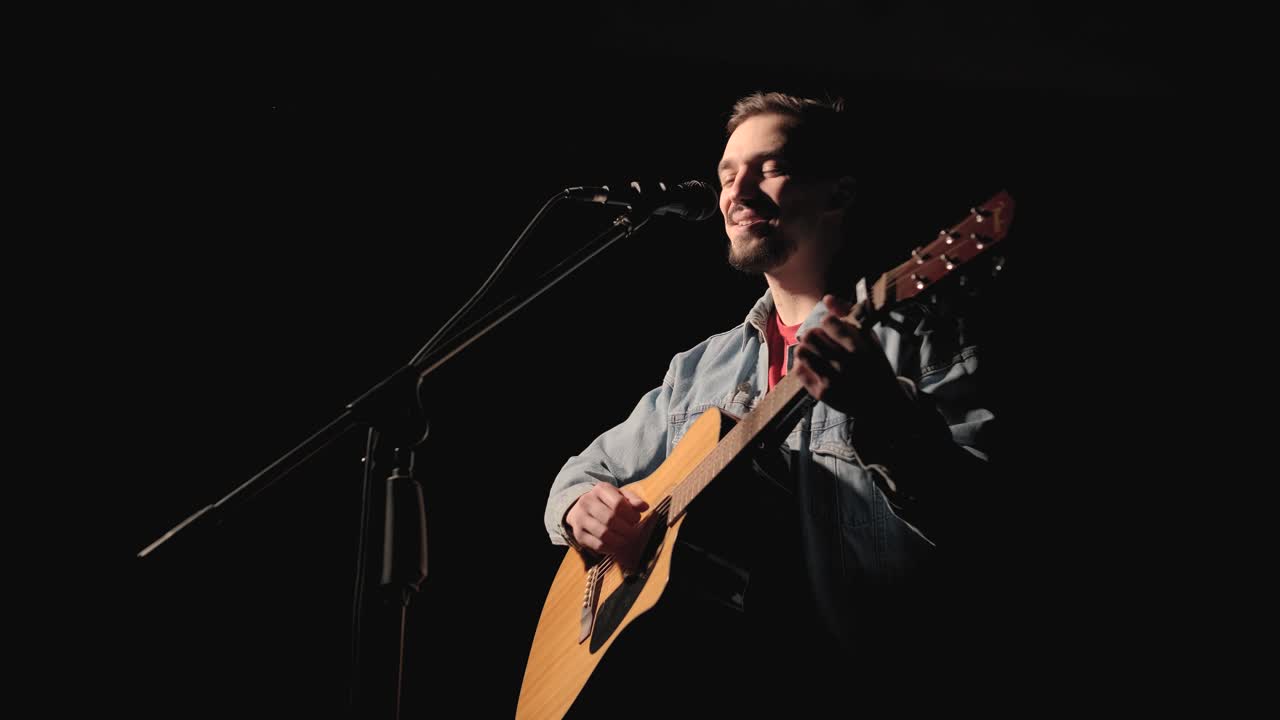 un músico está tocando la guitarra en un gran escenario con miembros de la audiencia sosteniendo linternas en el fondo. el auditorio está lleno de hermosas luces parpadeantes.