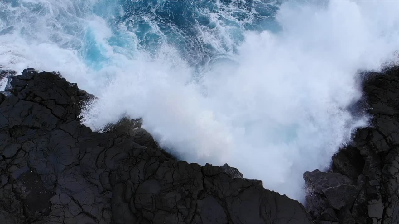 Waves meeting black rock volcanic cliffs birds pov