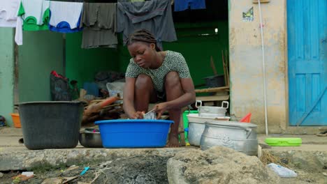 Local-woman-doing-her-household-chores-of-washing-dishes,-in-front-of-her-house-in-a-village-in-Kumasi,-Ghana,-Africa