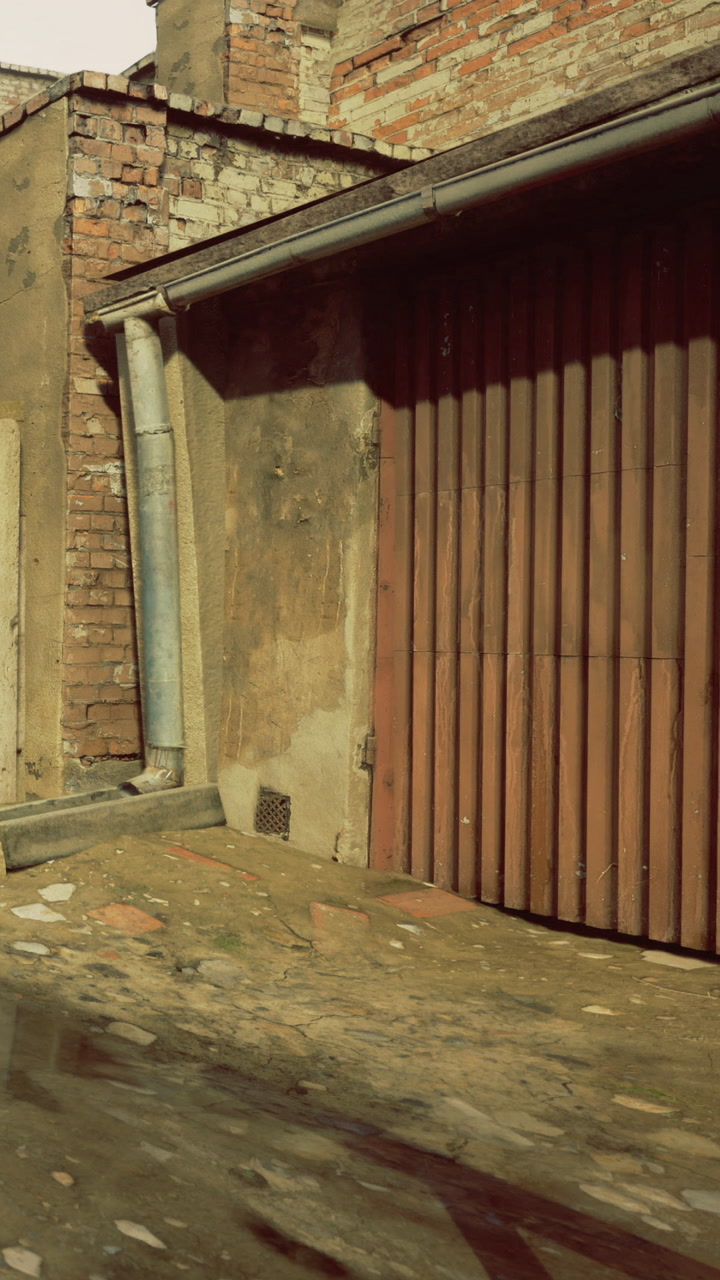 Old brick wall and drainage pipe in an alley with wet ground after rain