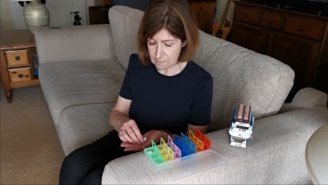 woman on couch fill her seven day medication into a colored pill box