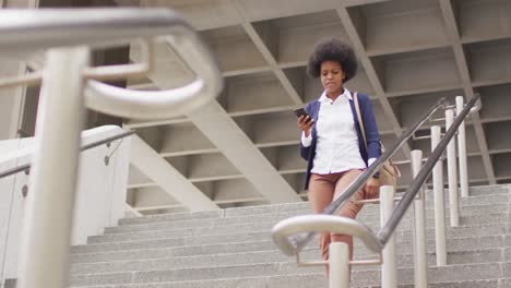 african american businesswoman walking and holding smartphone