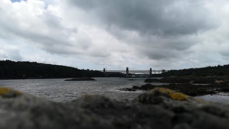 looking over unfocused rocky foreground to overcast menai straits britannia bridge to anglesey