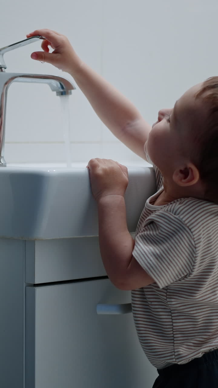 Caucasian toddler closes the tap. Kid touches water in the sink. Child ...