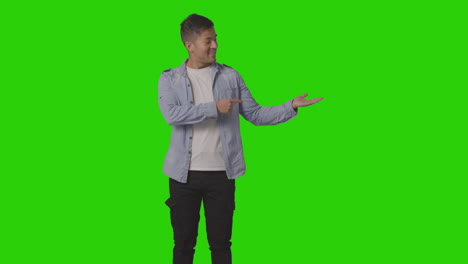 three quarter length studio shot of casually dressed young man presenting or showing against green screen