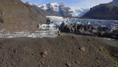 antena: toma lateral de un hombre caminando sobre una colina cerca del glaciar svinafellsjokull durante un día soleado