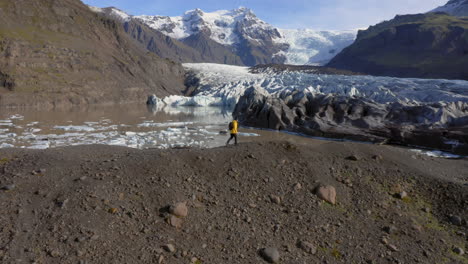 aerial: side follow shot of one man walking on a hill near svinafellsjokull glacier during a sunny day