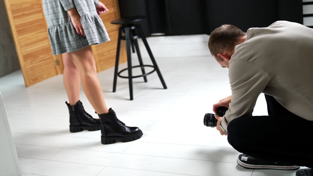 Backstage work of a fashion photo session in modern studio. Photographer takes a shot of a model sitting on the floor.