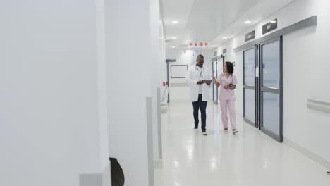 busy diverse doctors using tablet and talking in hospital in slow motion