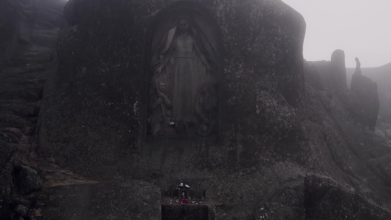 Statua di Nossa Senhora da Boa Estrela scolpita in una nicchia di granito nella Serra da Estrela, Portogallo, emerge da una parete rocciosa aspra con texture invecchiata e simbolismo sacro in un ambiente montano nebbioso.