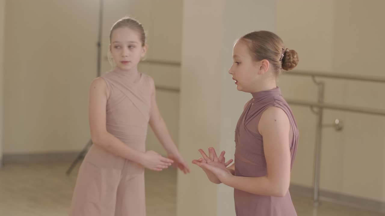 검은색 댄스웨어를 입은 젊은 발레 학생들이 나무 바닥과 벽에 장착된 바를 가진 넓은 발레 스튜디오에서 자세를 연습하는 그룹.