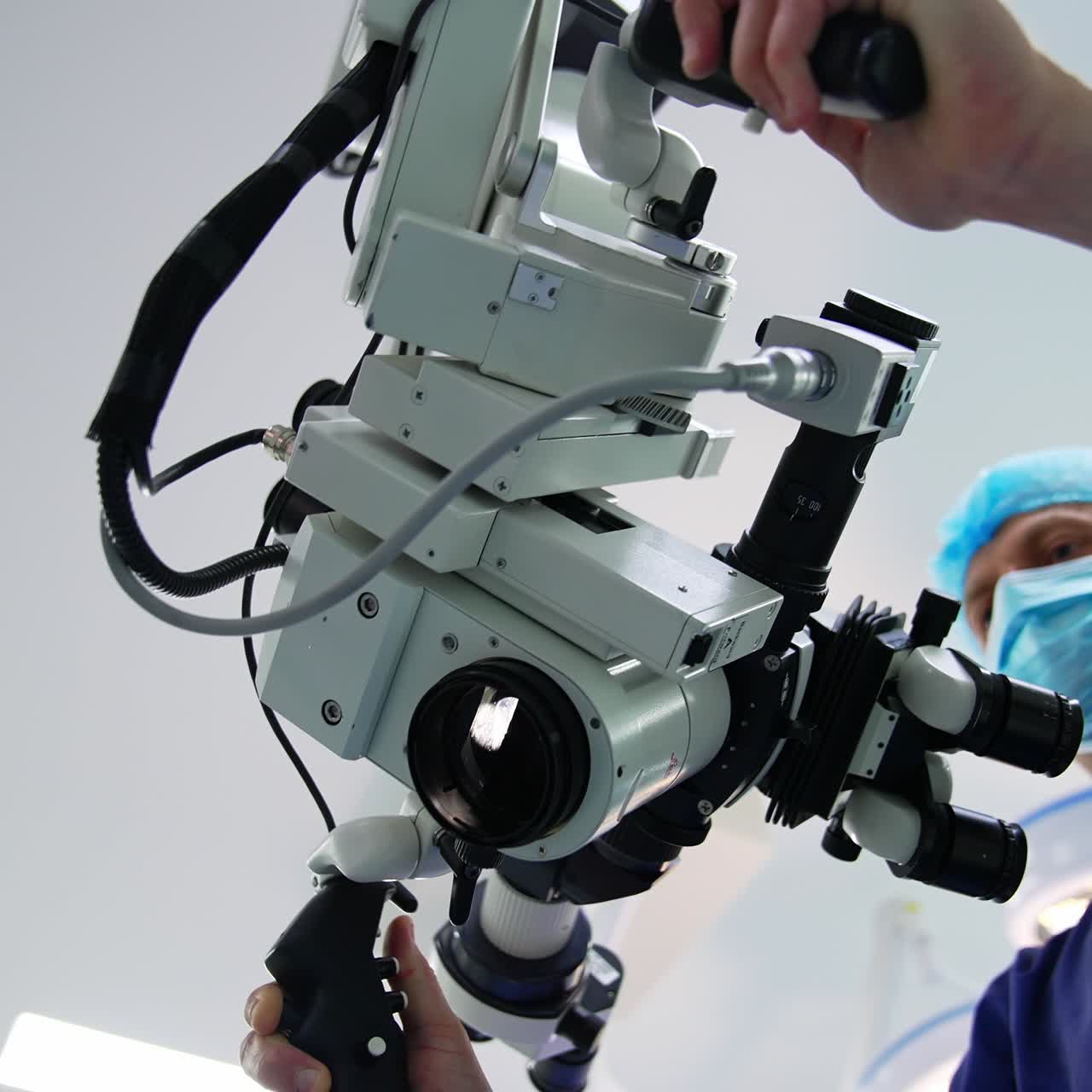 Confident professional surgeon rotating the microscope in surgery room. Doctor using technological equipment in modern surgery. Low angle view