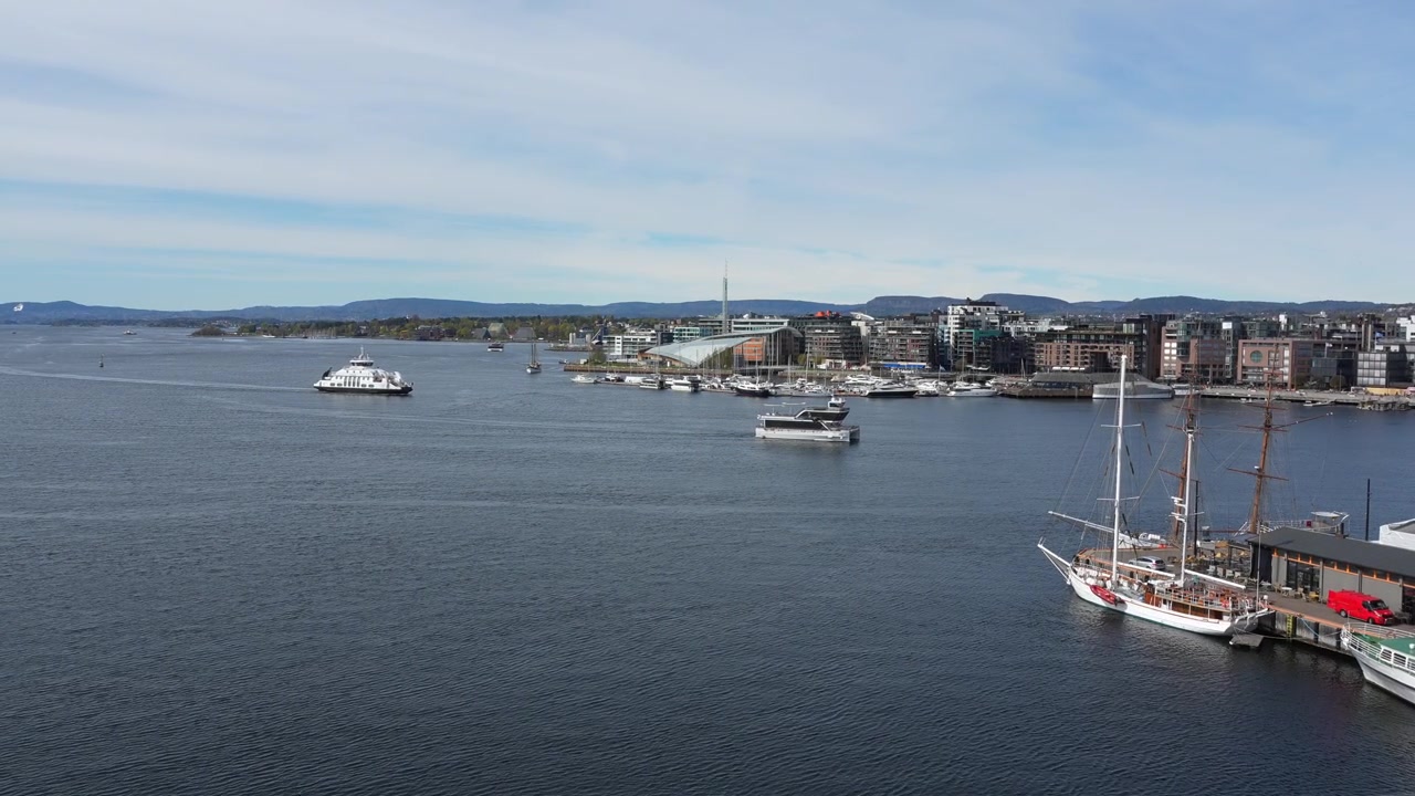 Handgehaltene Weitwinkelaufnahme zeigt Boote und Yachten, die auf dem Oslofjord segeln, vom Dach des Opernhauses aus gesehen, mit moderner Stadtlandschaft, klarem Himmel, dynamischem Wasser und gestochen scharfer natürlicher Beleuchtung.