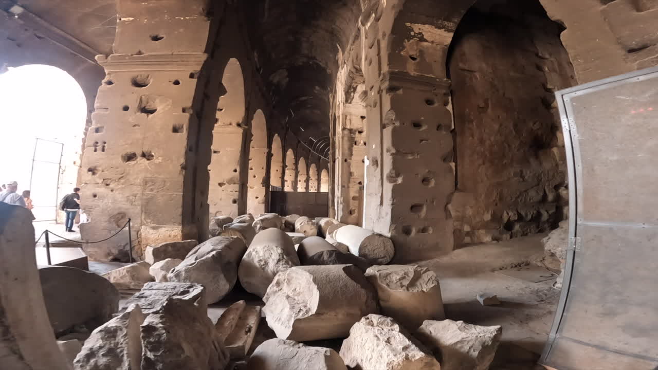 Pasaje subterráneo atmosférico en un antiguo yacimiento arqueológico romano que presenta columnas de piedra desgastadas, arcos de ladrillo y muros desmoronados.